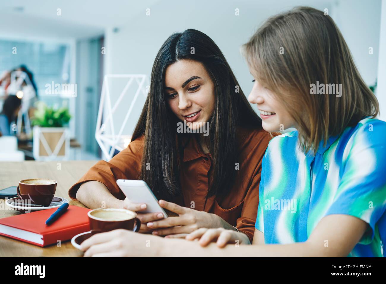 Femmes assis dans un café avec un café et un ordinateur portable utilisant un smartphone Banque D'Images