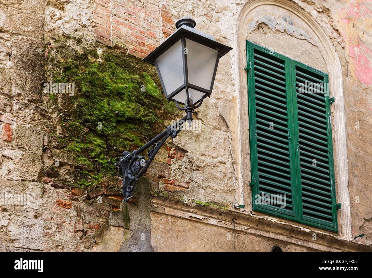 Une célèbre lanterne de rue sur un vieux mur avec de la mousse verte à Asciano, province de Sienne Banque D'Images