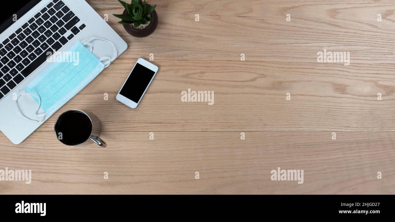 Bureau en chêne bureau table avec ordinateur portable, masque facial personnel, smartphone, plante pour bébé et café pour le travail ou l'école pendant le Covid pande Banque D'Images