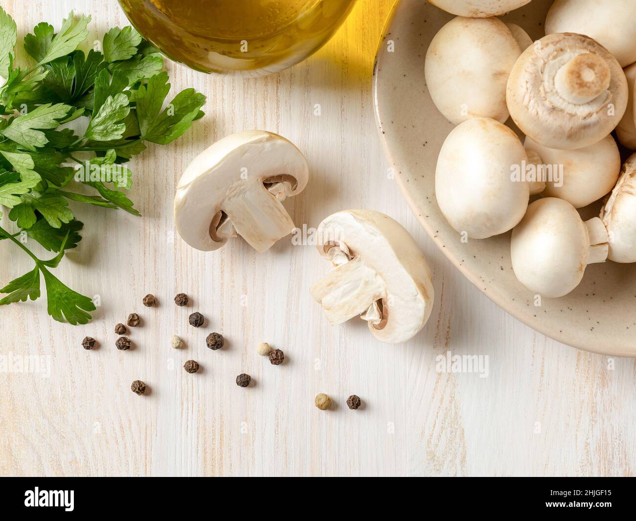 Couper dans du champignon à moitié cru près du persil frais, des champignons de Paris entiers et du pot d'huile d'olive sur une table en bois blanc.Concept de l'ingrédient alimentaire végétarien Banque D'Images