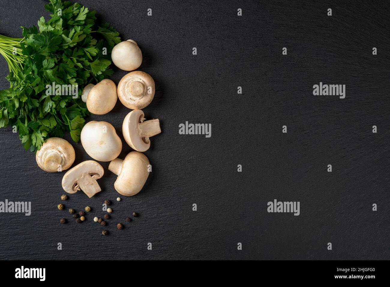 Champignons crus et coupés en deux et bouquet de persil sur une dalle d'ardoise noire.Cuisson de champignons de Paris frais Agaricus bisporus.Menu végétarien. Banque D'Images