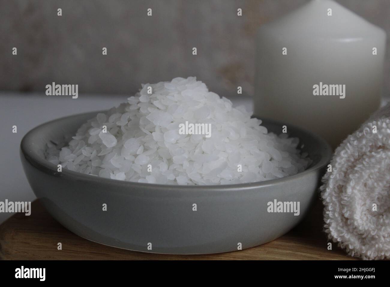 sel pour le bain gommage soins du corps à domicile.Le gros sel se trouve  dans une assiette de bol grise avec une cuillère en bois serviette bougie  sur fond gris.Détente au spa
