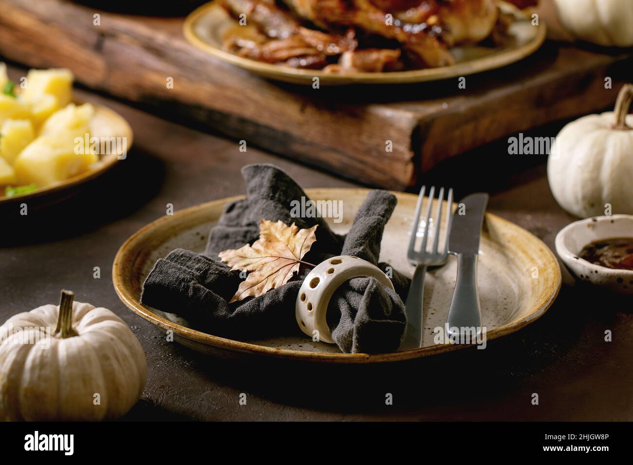 Table de fête avec plats classiques canard glacé rôti avec pommes, pommes de terre bouillies et sauce, plaque en céramique vide avec serviette et feuille d'automne Banque D'Images