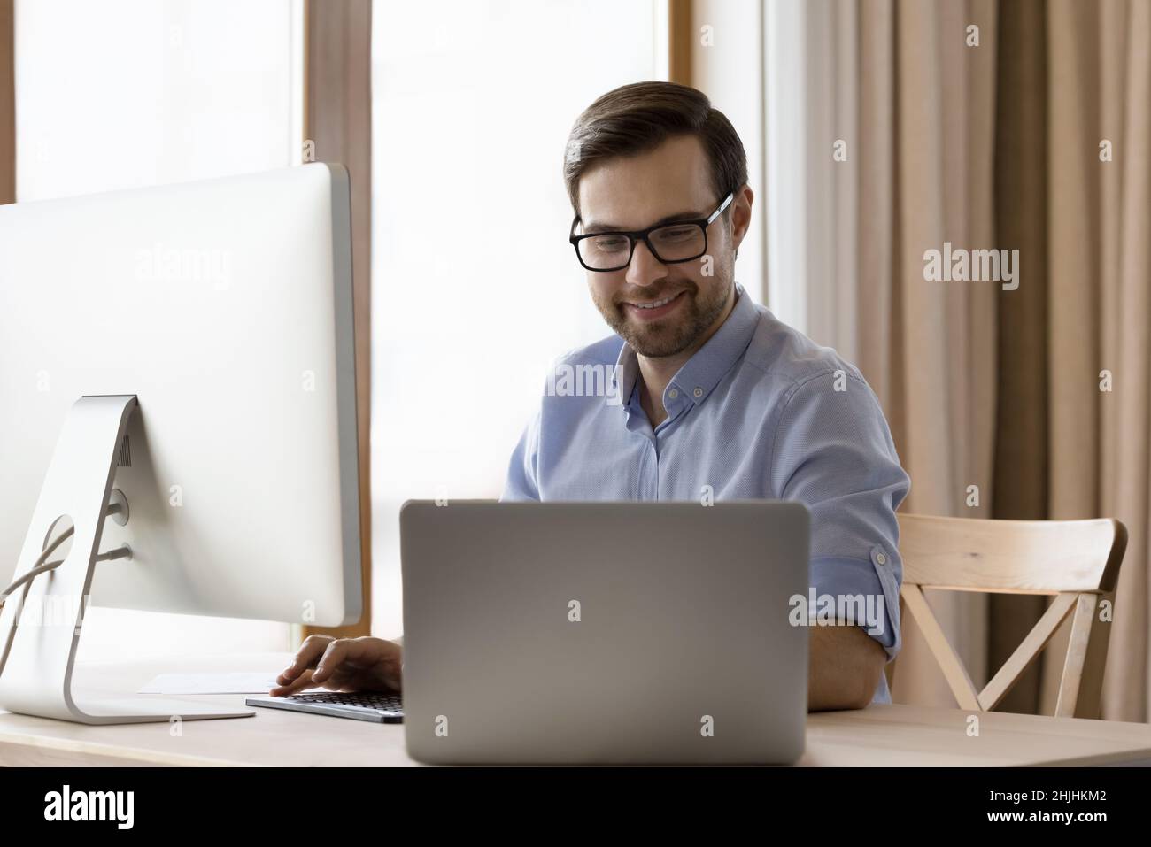 Joyeux homme d'affaires millénaire en lunettes de vue travaillant sur différents gadgets. Banque D'Images