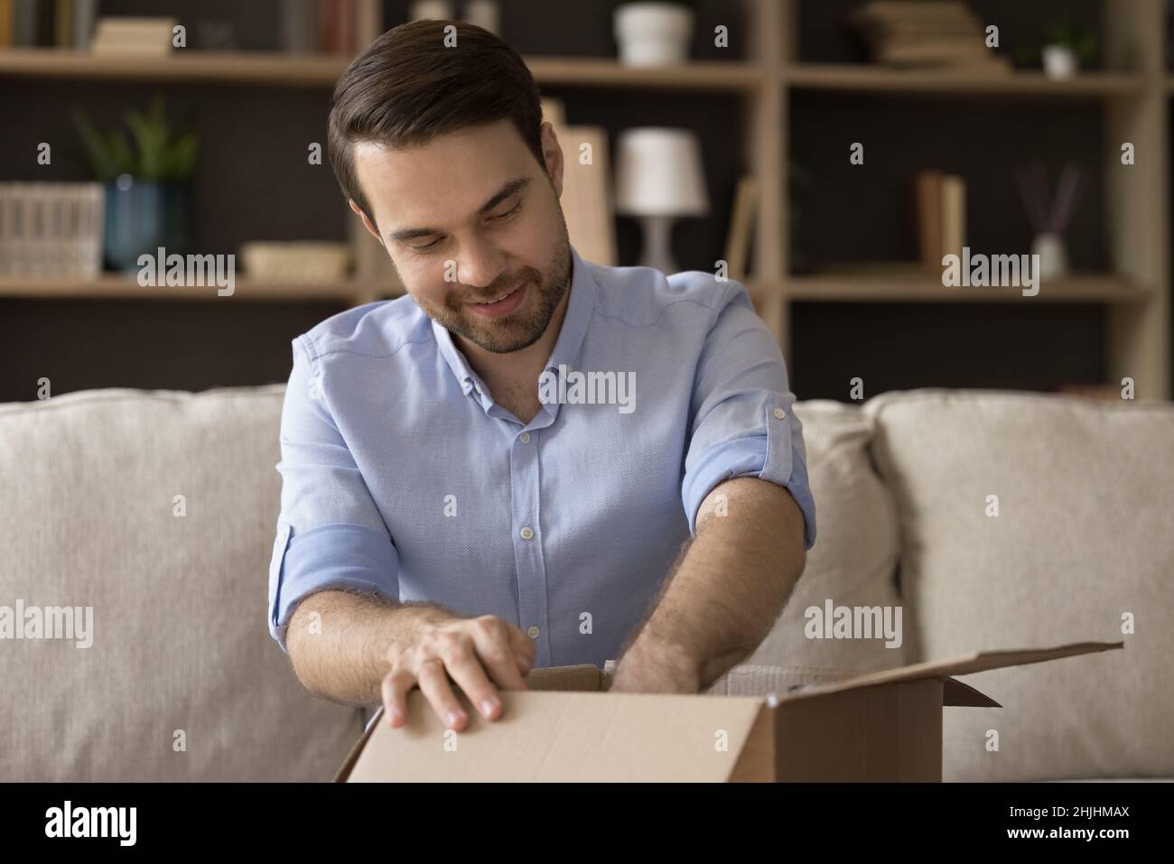 Curieux souriant jeune homme déballage boîte carton. Banque D'Images