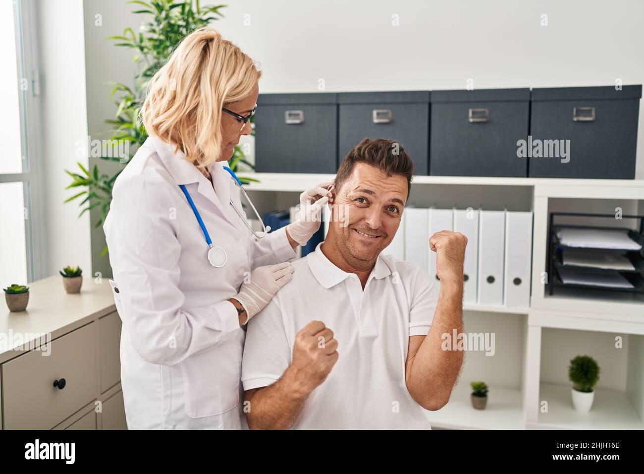Homme hispanique qui obtient une aide auditive médicale chez le médecin criant fier, célébrant la victoire et le succès très excité avec les bras levés Banque D'Images