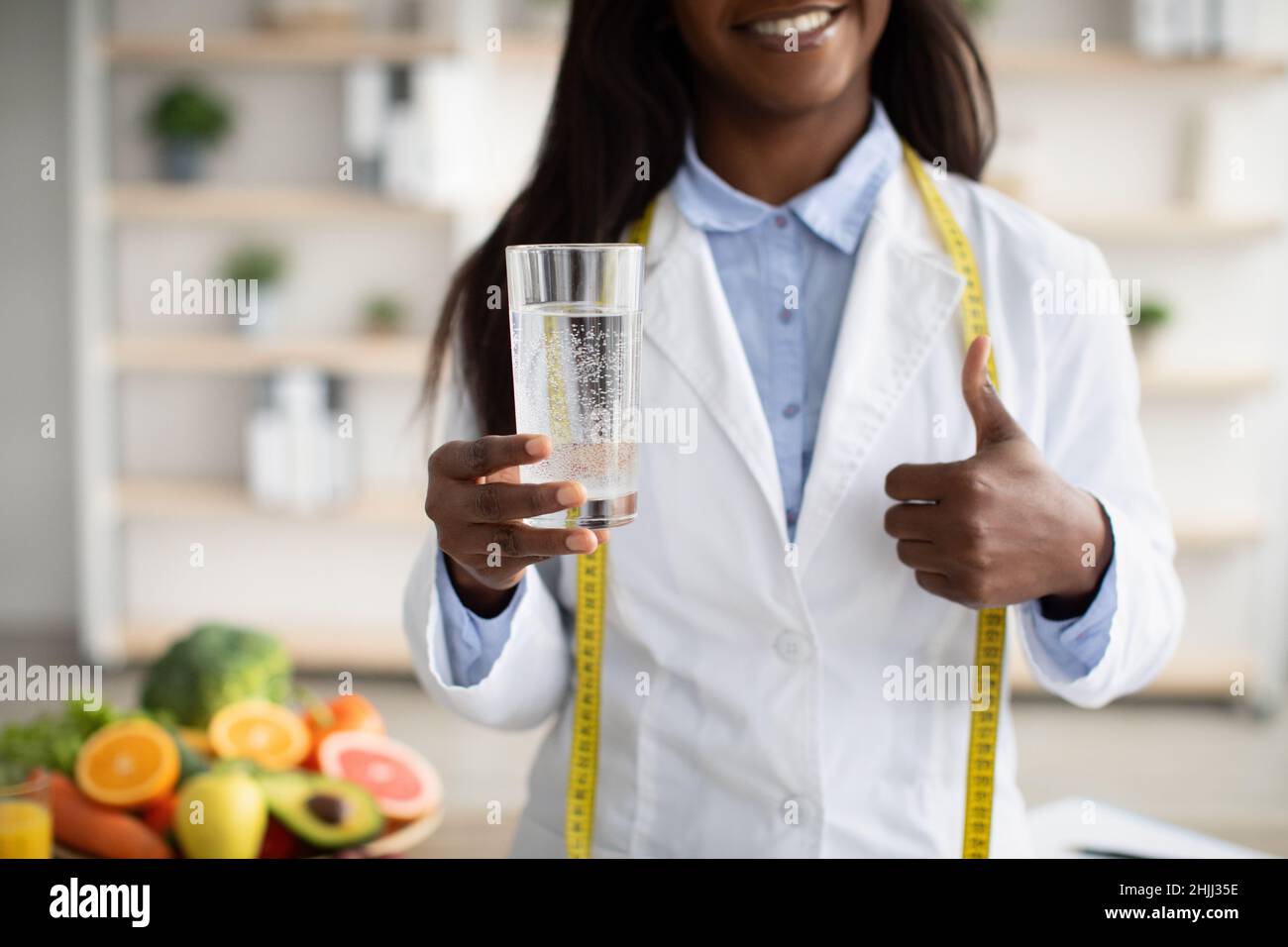 Détox et concept de nettoyage.Femme afro-américaine nutritionniste tenant un verre d'eau et montrant le pouce vers le haut Banque D'Images