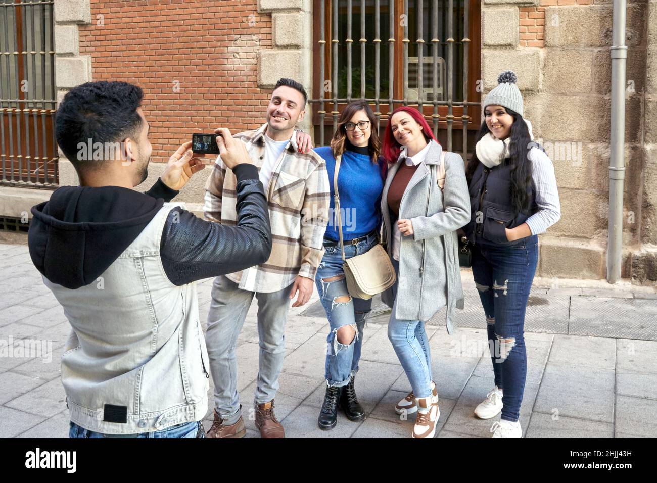 Latino homme prenant une photo avec son smartphone de son groupe d'amis dans une rue de ville. Banque D'Images