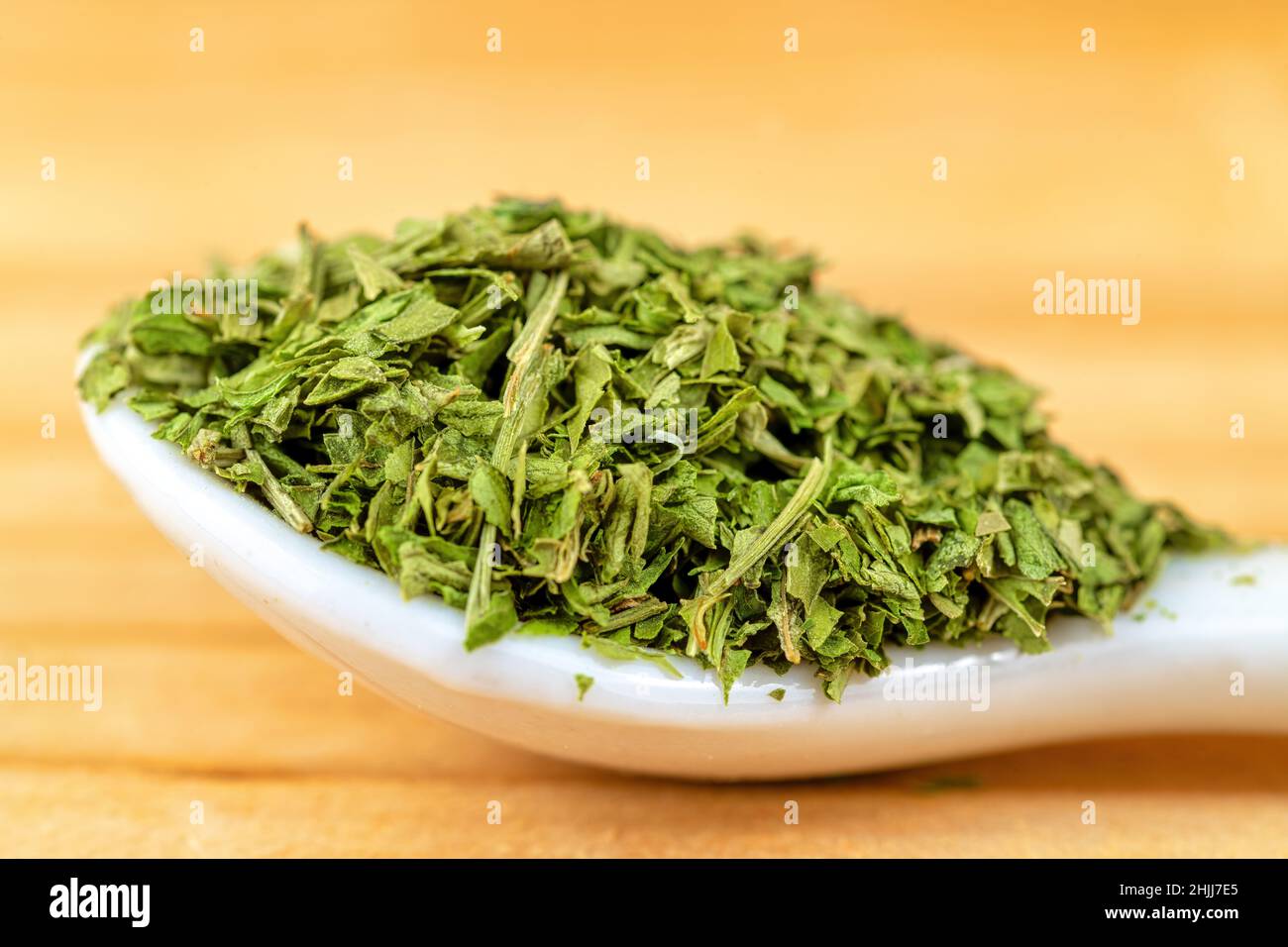 Cuillère en céramique à gros plan avec tas d'herbes vertes séchées placées sur une table en bois dans la cuisine Banque D'Images