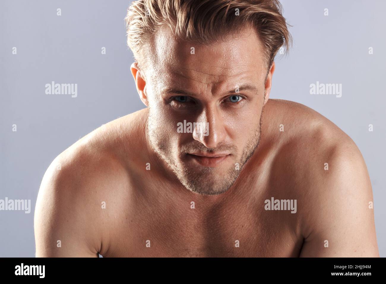 sexy caucasien homme blond avec les yeux bleus et pompé vers le haut muscles athlétiques, l'homme est habillé en jeans et un t-shirt blanc dans un studio de photo un Banque D'Images