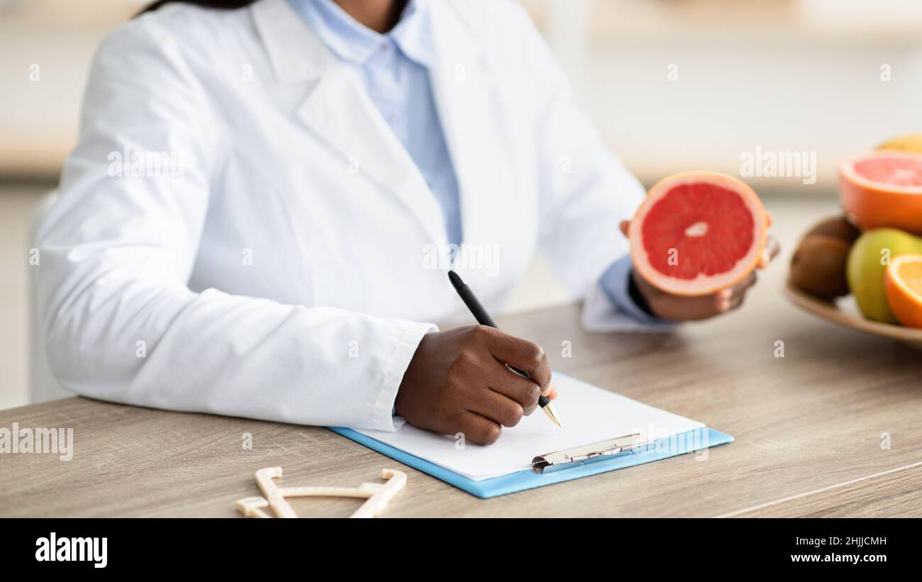 Nutritionniste afro-américaine tenant le pamplemousse, faisant le plan de repas pour le client à la clinique de perte de poids, gros plan Banque D'Images