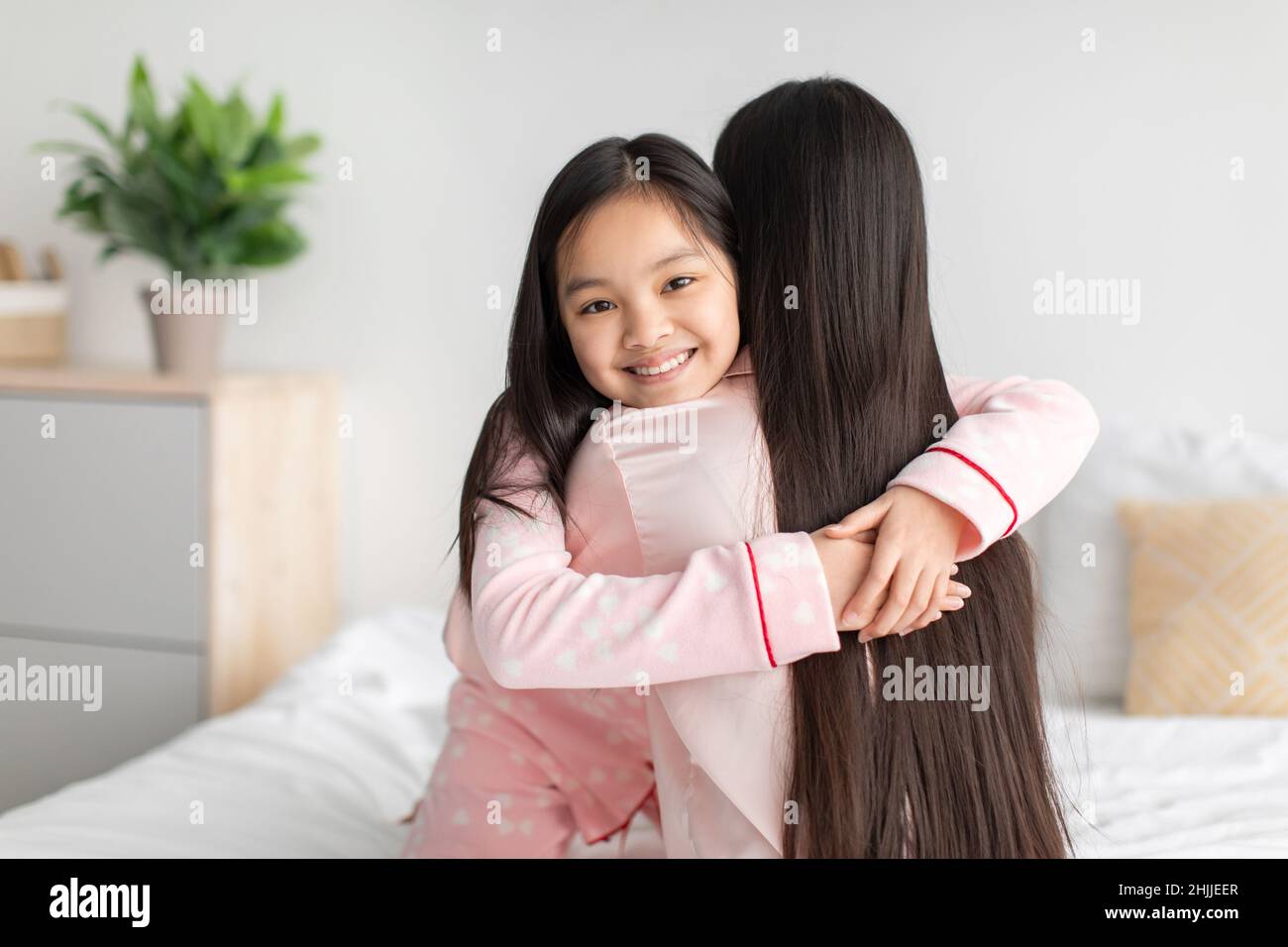 Satisfaite heureuse jeune fille chinoise embrassant une jeune femme sur le lit dans la chambre à coucher à l'intérieur, espace libre Banque D'Images