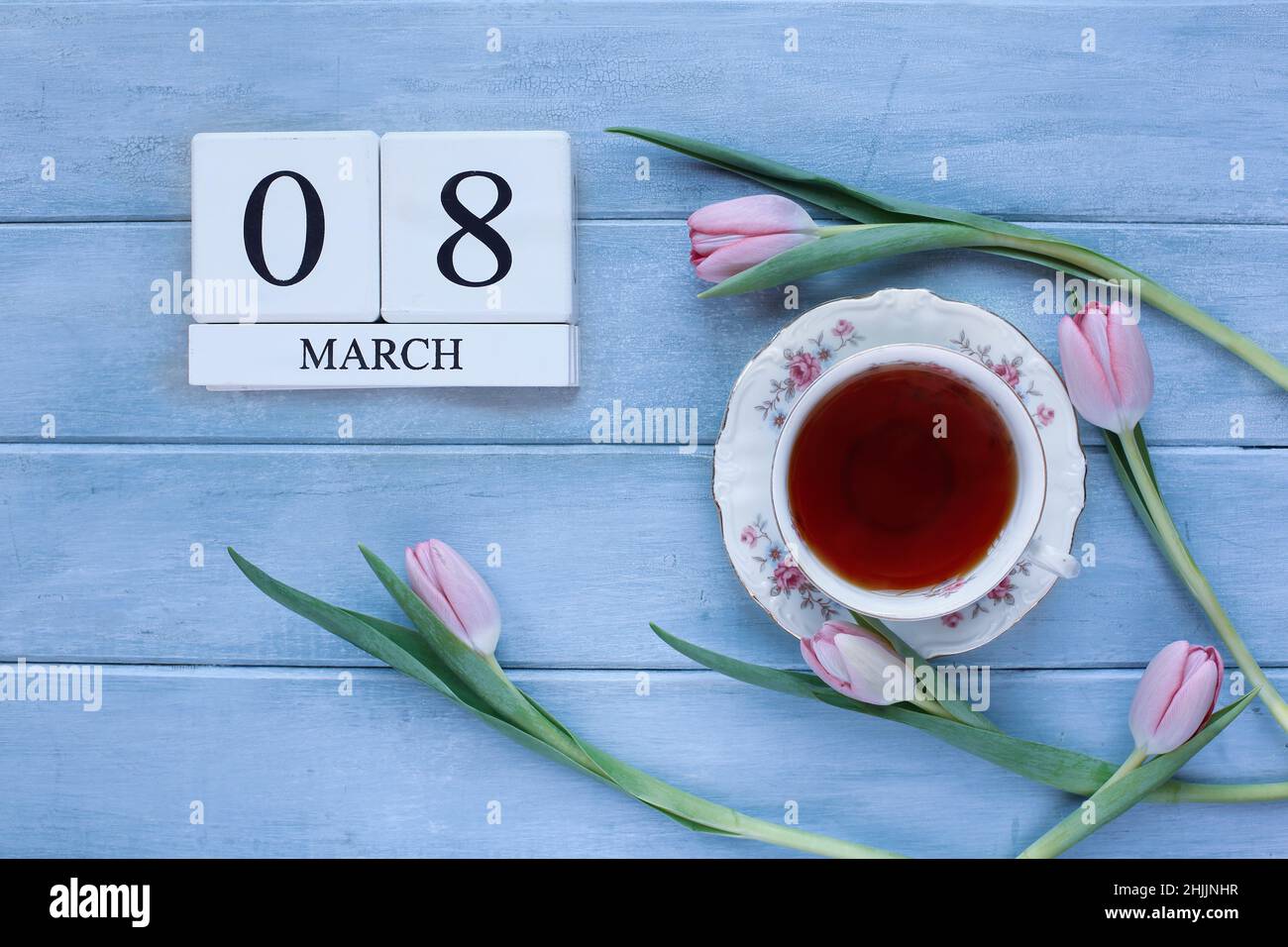 Des blocs de calendrier en bois blanc avec la date du 08 mai et des fleurs de tulipe roses avec du thé sur fond de bois bleu pour la Journée des femmes. Banque D'Images