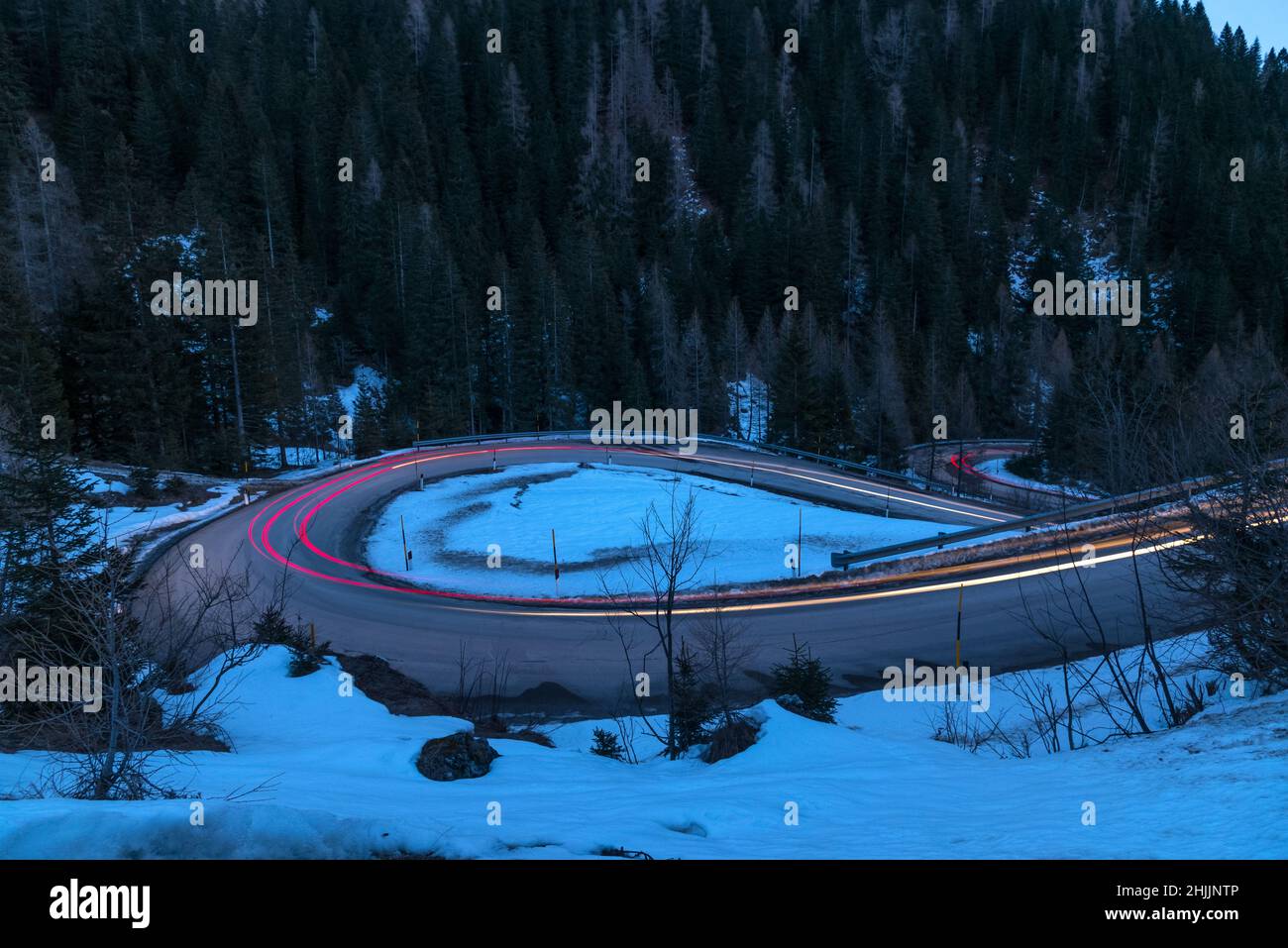 Sentiers légers sur une route sinueuse dans les Alpes européennes au crépuscule en hiver Banque D'Images