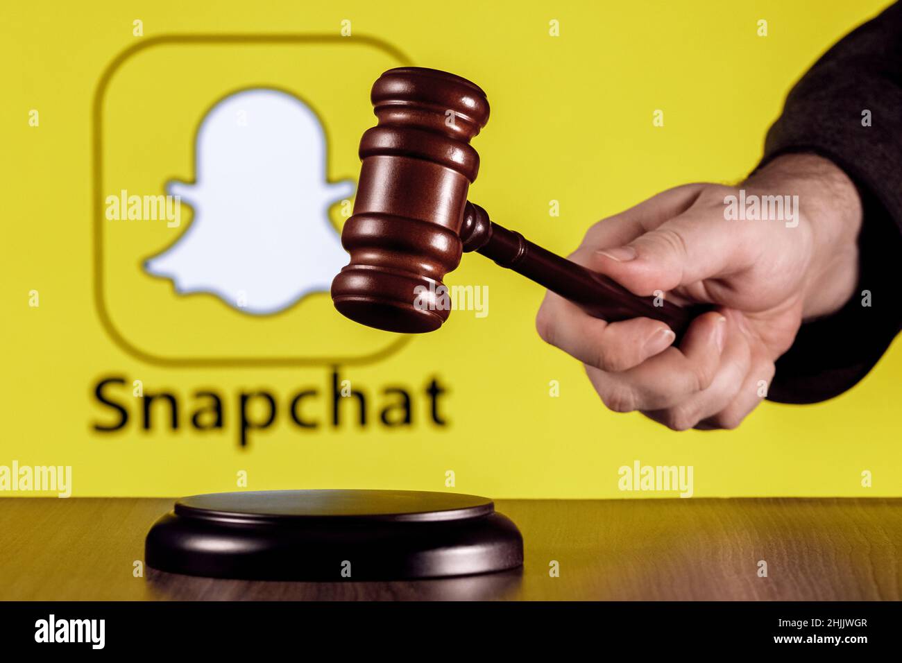 Gavel à portée de main sur l'arrière-plan du logo du service de messagerie instantanée Snapchat. Le concept du procès. Banque D'Images