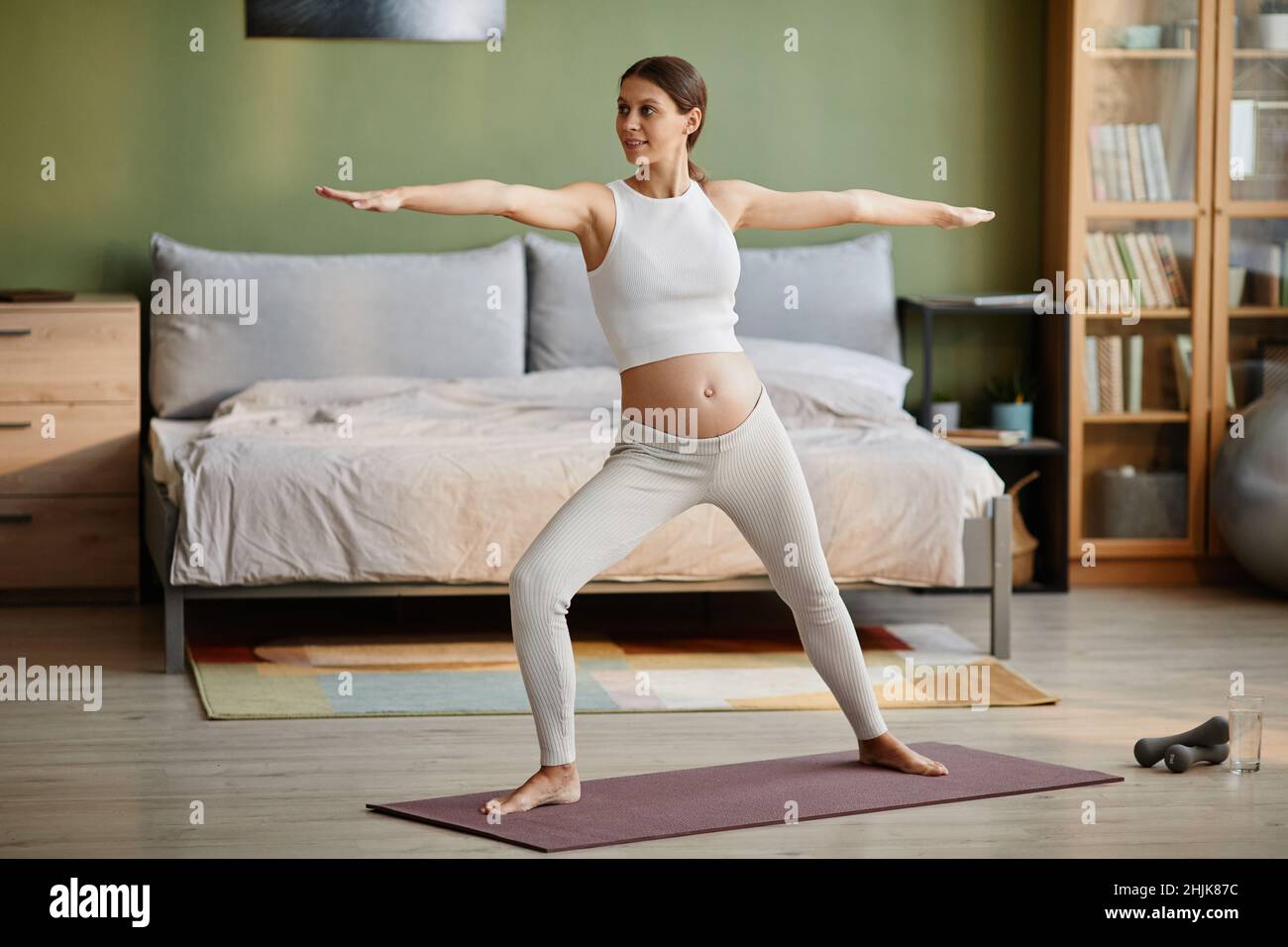 Jeune femme enceinte debout sur un tapis d'exercice et faisant des exercices d'étirement le matin dans sa chambre Banque D'Images