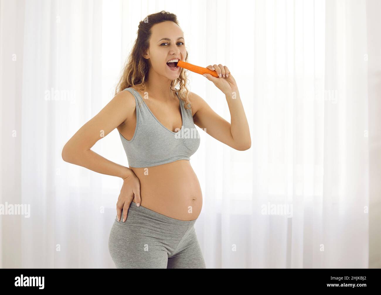 Portrait d'une jeune femme enceinte souriante qui aime manger des carottes pendant la grossesse. Banque D'Images