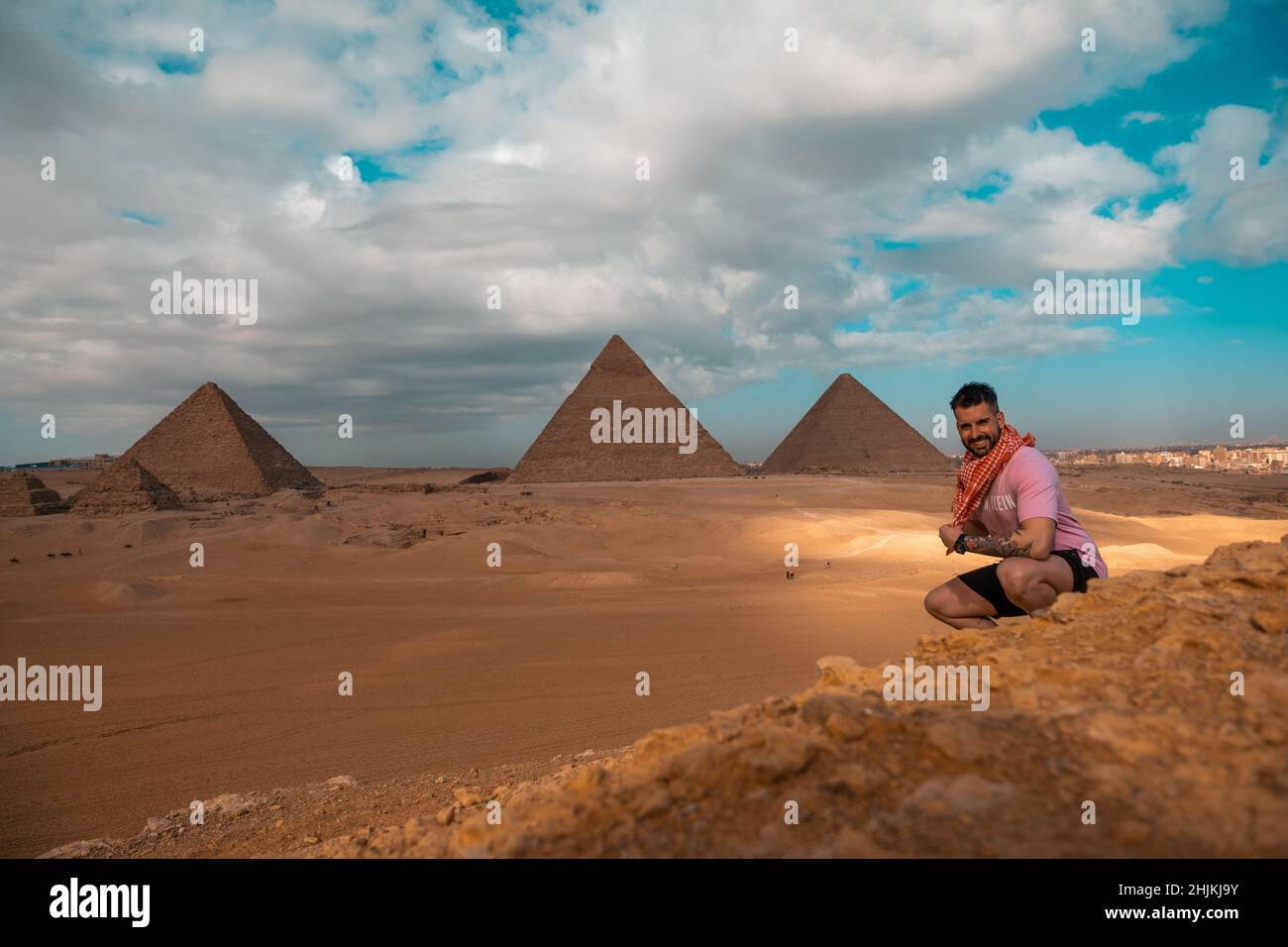 Homme assis sur les dunes de sable du désert se posant devant les grandes pyramides de gizeh.Voyager en egypte en hiver, les touristes posant pour une photo Banque D'Images