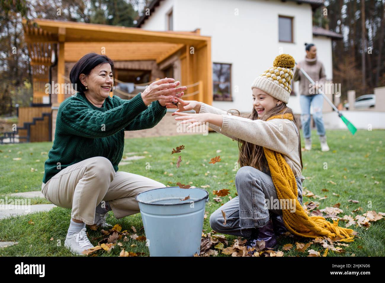 Bonne petite fille avec grand-mère ramasser les feuilles et les mettre dans le seau dans le jardin en automne Banque D'Images