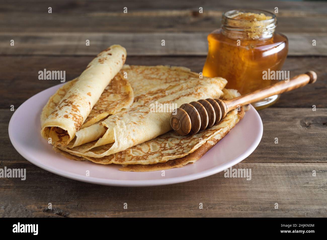 Crêpes au miel sur fond de bois sur assiette rose avec cuillère à miel.Copier l'espace. Banque D'Images