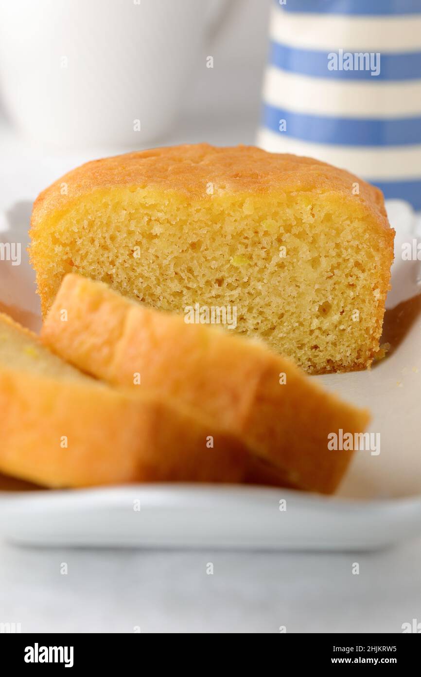Gâteau fait maison pour le thé de l'après-midi, coupé en tranches sur une assiette rectangulaire blanche avec une carafe de style cornishware à rayures bleues et blanches à l'arrière-plan Banque D'Images