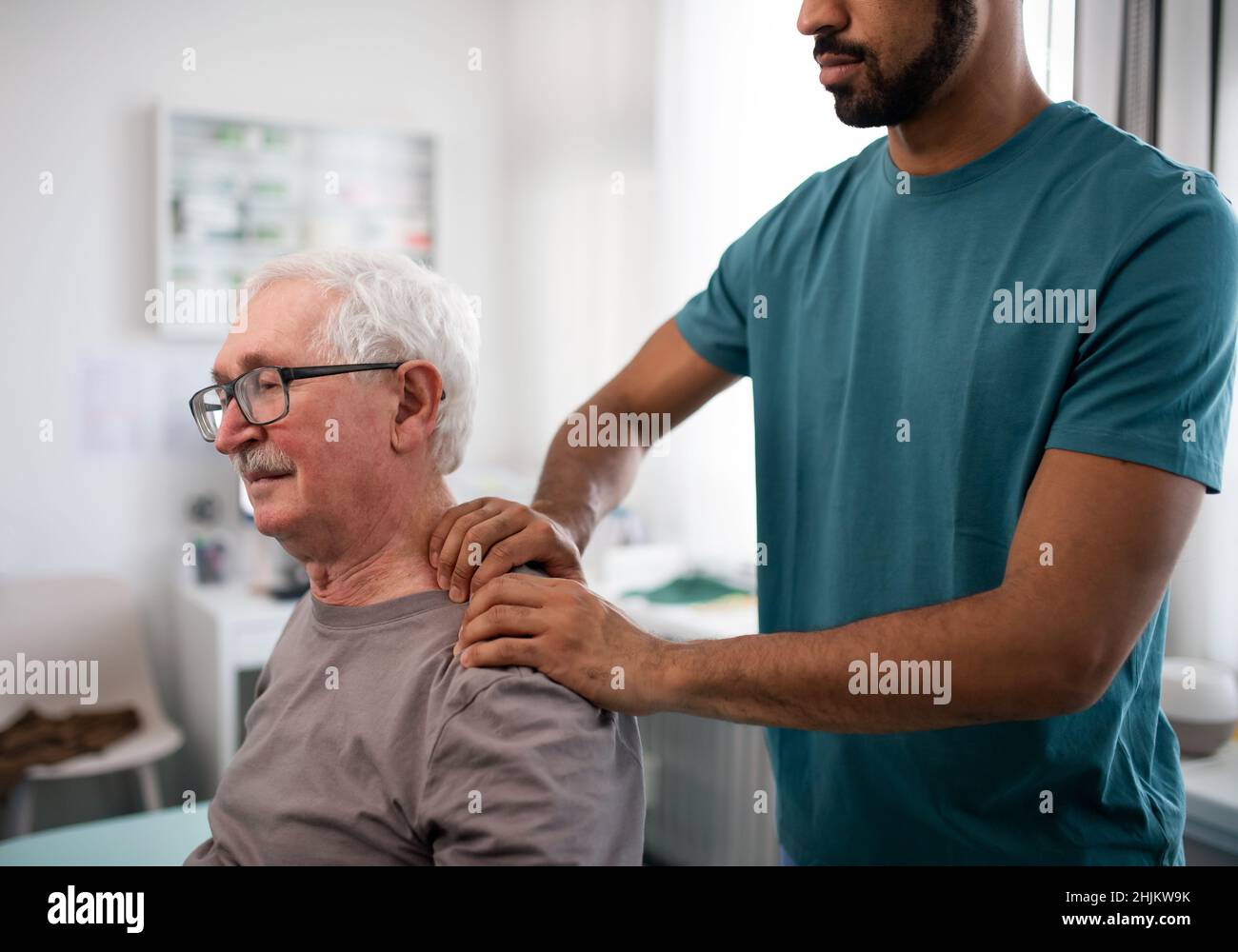 Un jeune kinésithérapeute massante le cou d'un patient âgé dans une salle de physiothérapie Banque D'Images
