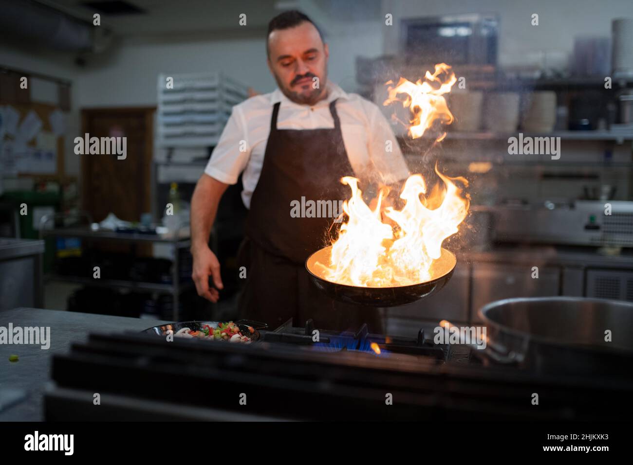Chef professionnel préparant des repas, flambant à l'intérieur dans la cuisine du restaurant. Banque D'Images