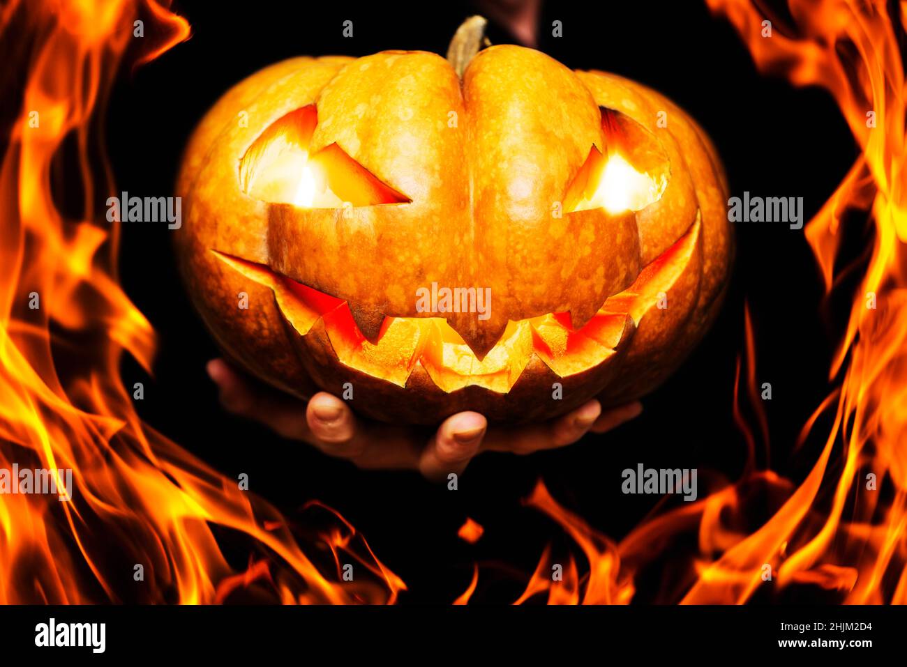 Feu autour de la citrouille d'Halloween avec les yeux et la bouche brûlants dans une main de homme.Main montre la citrouille d'halloween brûlante à travers les flammes.Bonne bannière Halloween Banque D'Images