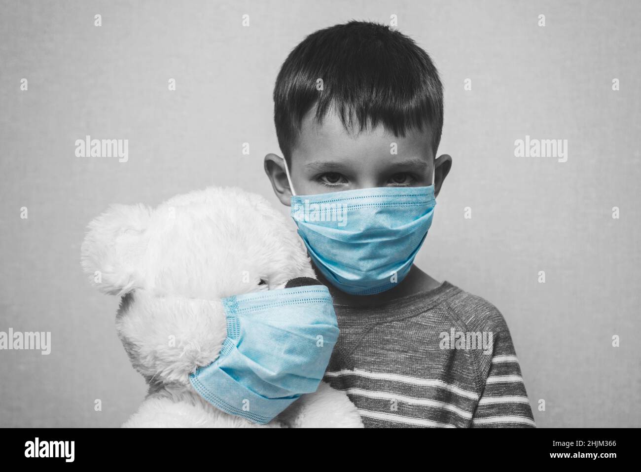 Un enfant triste tient son ours en peluche, tous deux portant des masques médicaux de protection.Quarantaine du coronavirus.Prévention épidémie. Banque D'Images