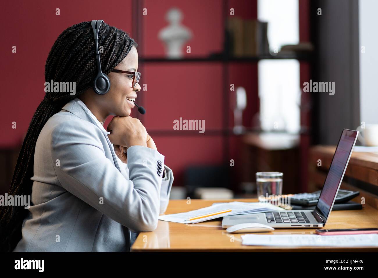 Jeune femme africaine souriante, mère en congé de maternité, dans un micro-casque sans fil, travaillant à distance de chez elle Banque D'Images