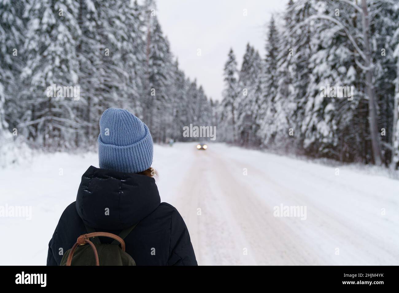 Femme voyageur regardant la distance à la voiture en mouvement en se tenant sur la route enneigée dans la forêt d'hiver Banque D'Images