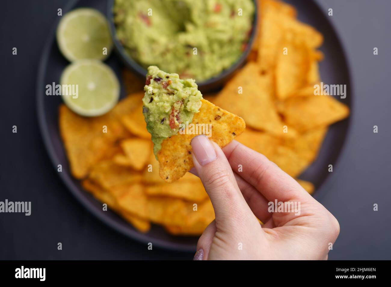 Gros plan de la main de femme avec des chips de tortilla ou nachos avec trempette fraîche et savoureuse de guacamole Banque D'Images