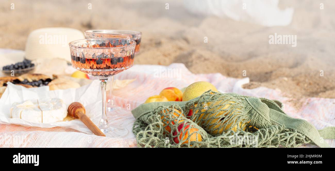 Magnifique pique-nique d'été au coucher du soleil sur la plage avec vin de rose, fromage, galette aux myrtilles et fruits frais.Copier l'espace Banque D'Images
