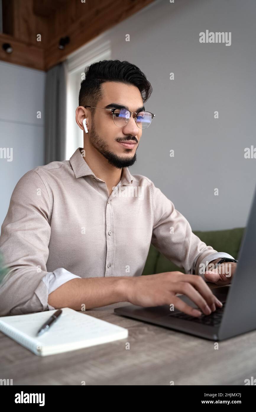 Un jeune homme heureux étudie ou travaille en ligne sur un ordinateur portable à partir d'un bureau à domicile Banque D'Images