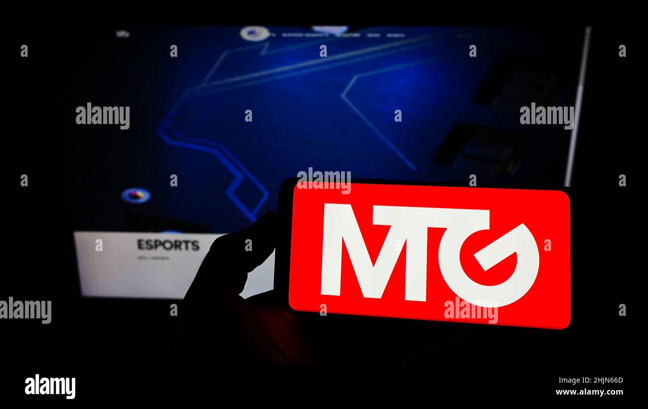 Personne tenant un smartphone avec le logo de la société suédoise Modern Times Group AB (MTG) à l'écran devant le site Web.Mise au point sur l'affichage du téléphone. Banque D'Images