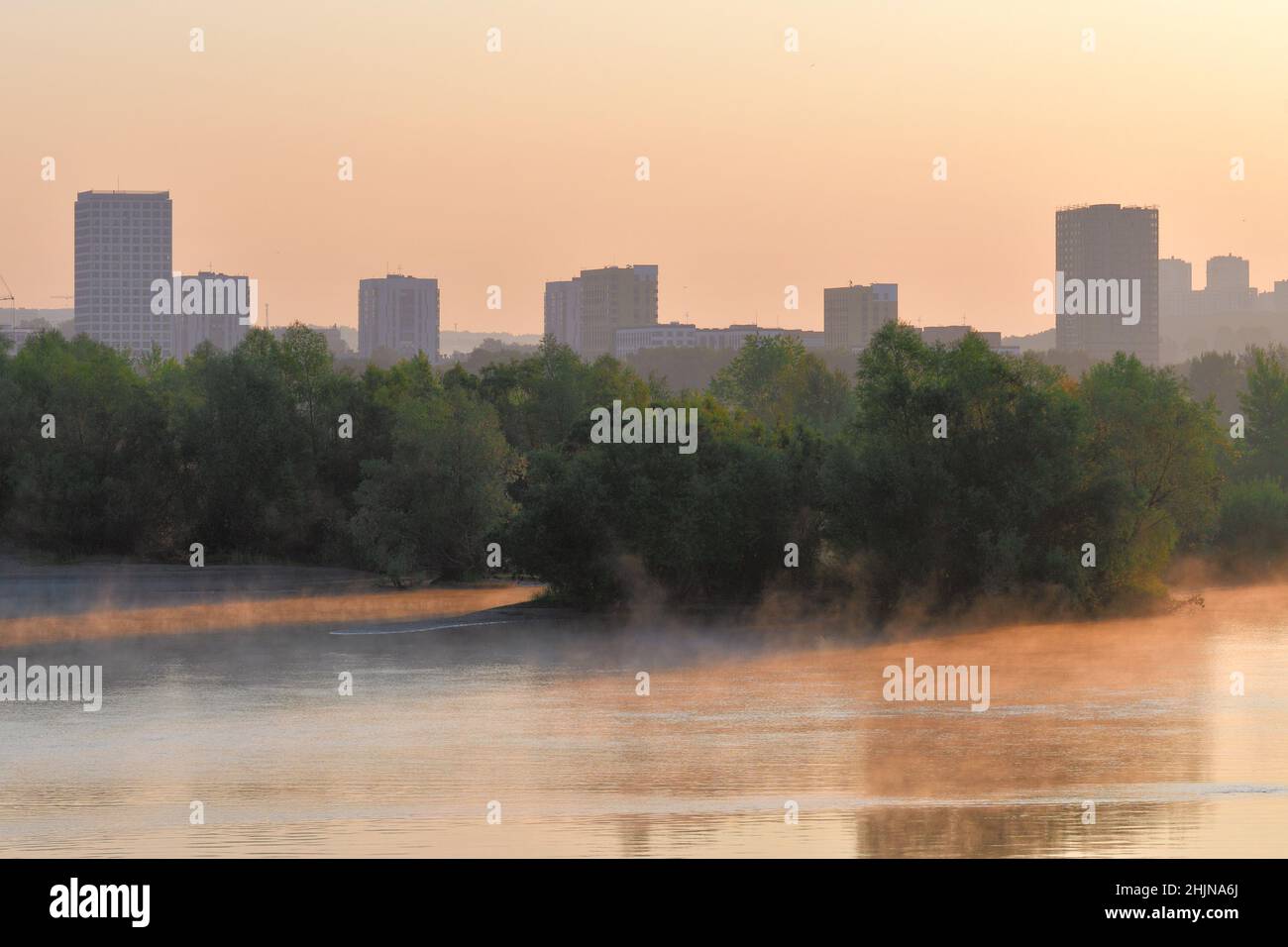 Maisons et arbres sur la rive de la rivière.Grandes maisons, arbres luxuriants sur la rive à l'aube.Brouillard sur l'eau, reflets dans l'eau, couleur rose.Novosi Banque D'Images