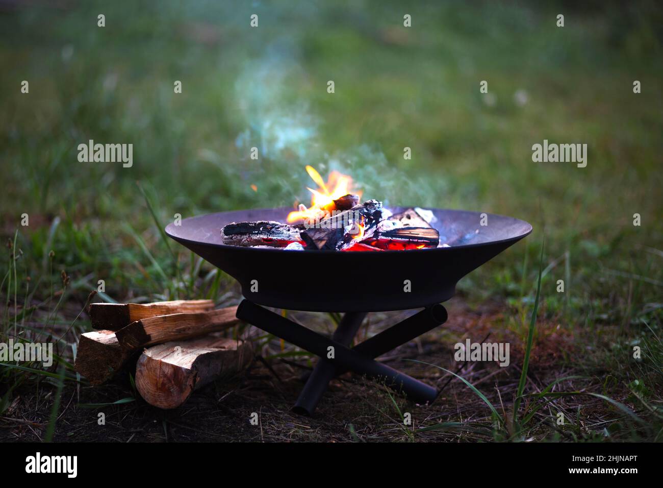 La flamme du feu brûle dans un foyer en métal - réchauffez vos mains par le feu, remuez le bois de chauffage avec un bâton.Un foyer de bois de chauffage pour un camping sûr Banque D'Images