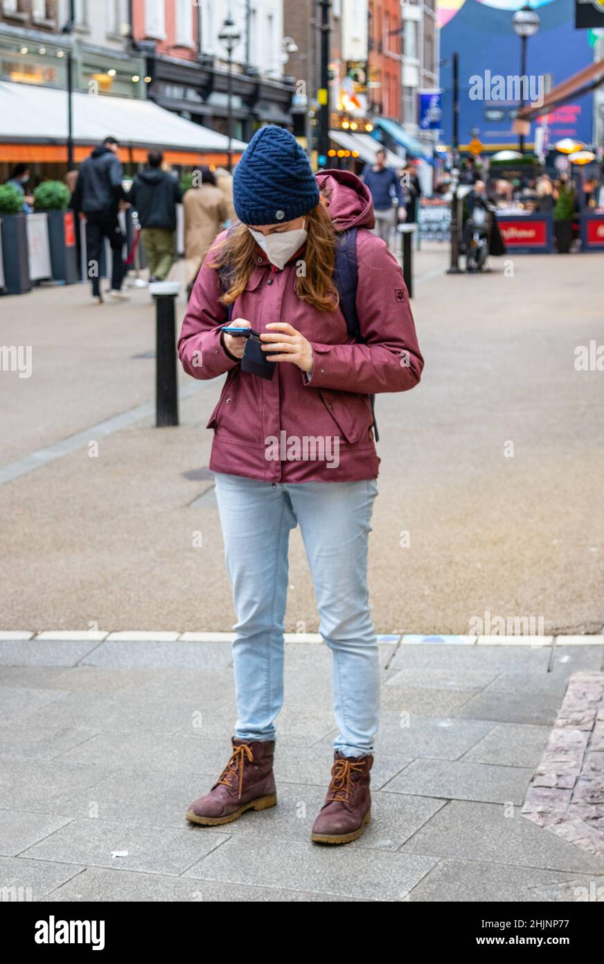 Jeune fille avec un masque facial dans une veste rouge utilise un  smartphone, voit les nouvelles, Grafton Street à l'heure du matin, pas de  personnes à proximité, Dublin, Irlande Photo Stock -