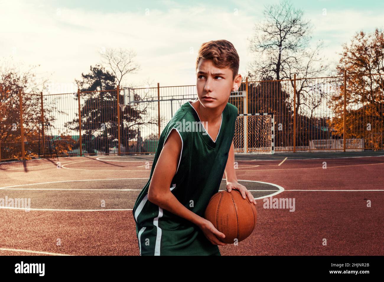 Sports et basket-ball.Un jeune adolescent dans un survêtement vert pose  avec un basket-ball dans ses mains et est prêt à lancer.En arrière-plan, un  basketba Photo Stock - Alamy