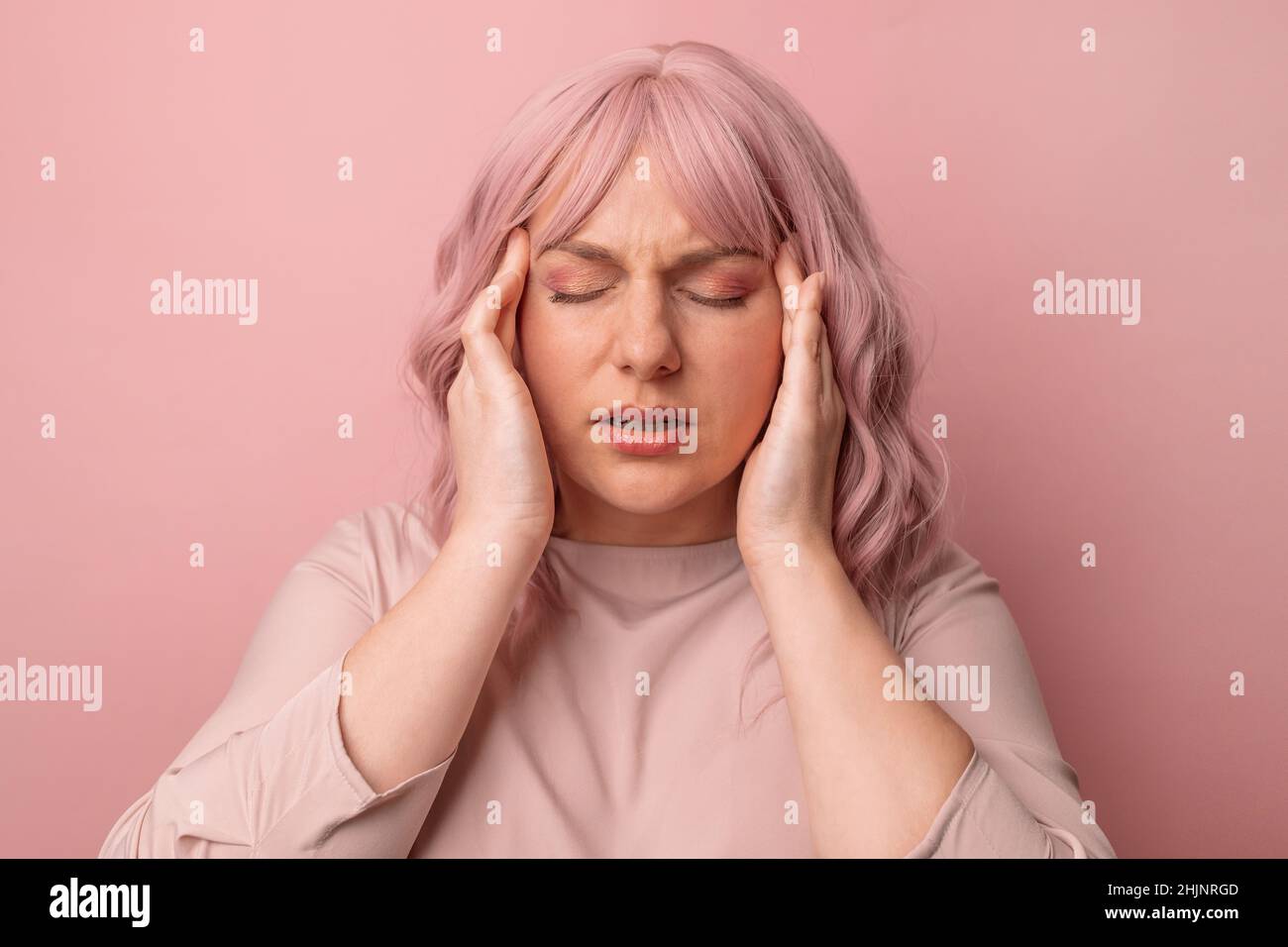 Jeune femme se sentant stressée sur fond rose.Souffrir de migraine. Banque D'Images