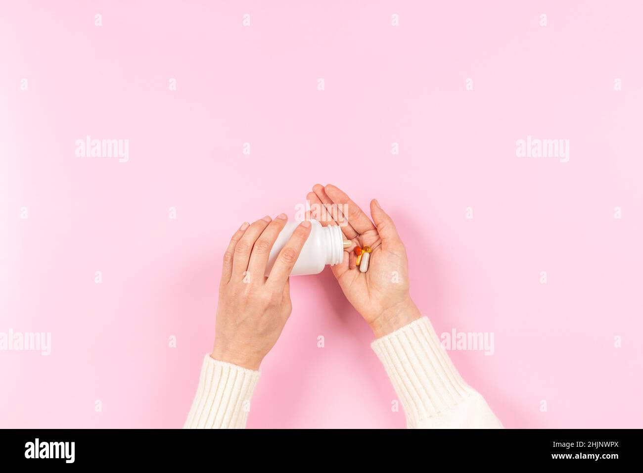 Pilules et capsules de médecine colorées dans la main de femme sur fond rose pastel.Les pilules de déversement de main de femme hors de la pharmacie de bouteille blanche, médecine et Banque D'Images