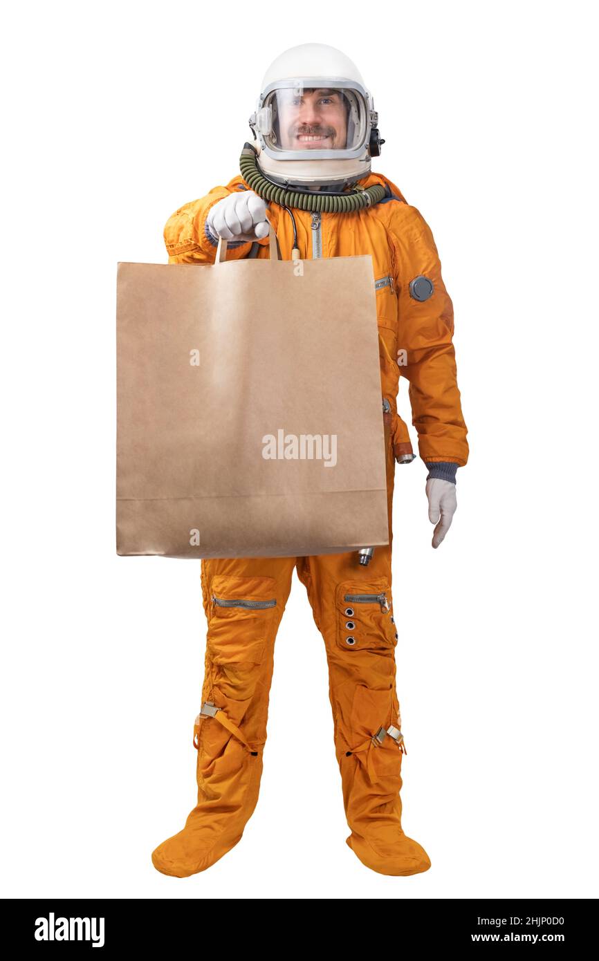 Un astronaute heureux portant un costume d'espace orange et un casque d'espace tenant à la main dans un sac en papier kraft vierge isolé sur fond blanc. Concept de livraison Banque D'Images