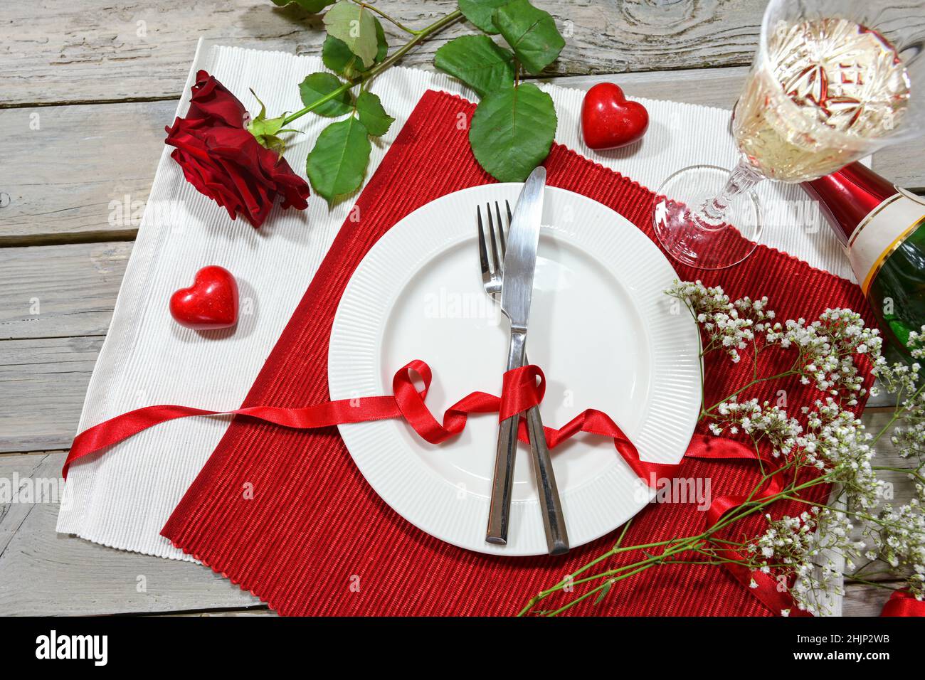 Table romantique avec une rose rouge, champagne et deux coeurs, assiette et couverts sur des serviettes rouges et blanches et une table rustique en bois, vue panoramique Banque D'Images