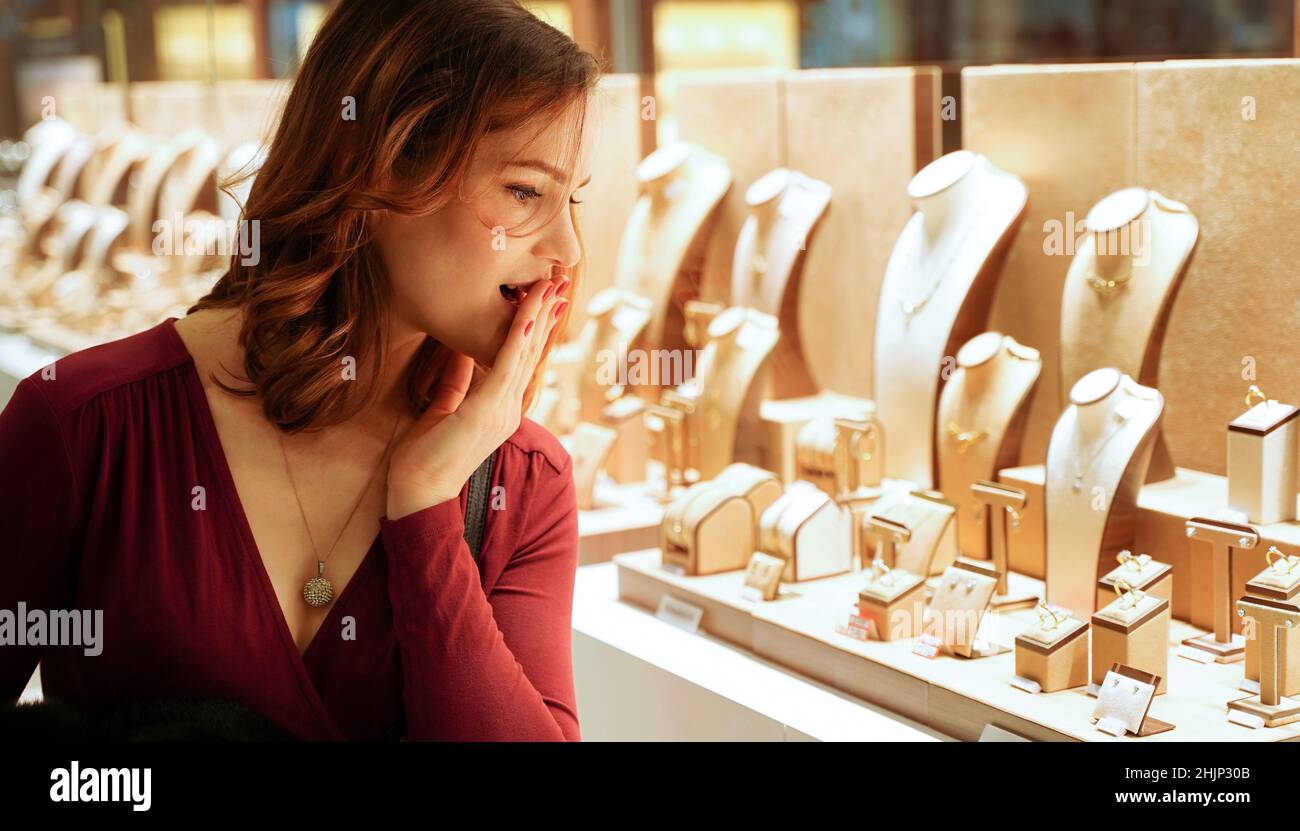 Surprise jolie femme regardant les bijoux dans la fenêtre du magasin.Fille près des bijoux.Le client intéressé choisit de l'or, des diamants ou des pierres précieuses.Achat Banque D'Images