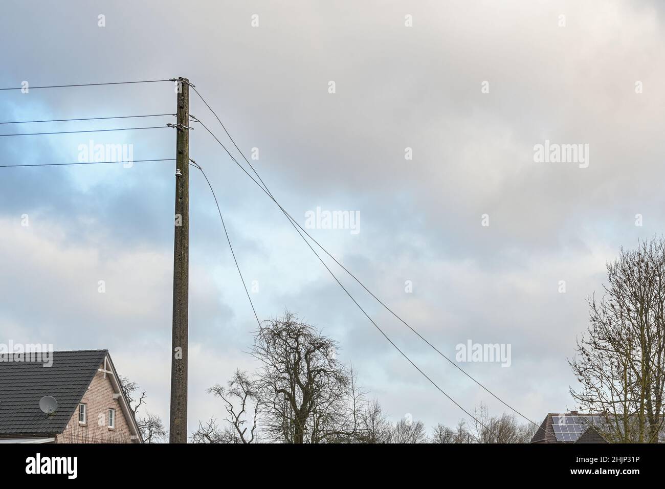 Poteau de puissance en béton avec lignes de transmission aériennes déchirées, dommages causés par une tempête dans un village rural, ciel nuageux avec espace de copie, focus sélectionné Banque D'Images