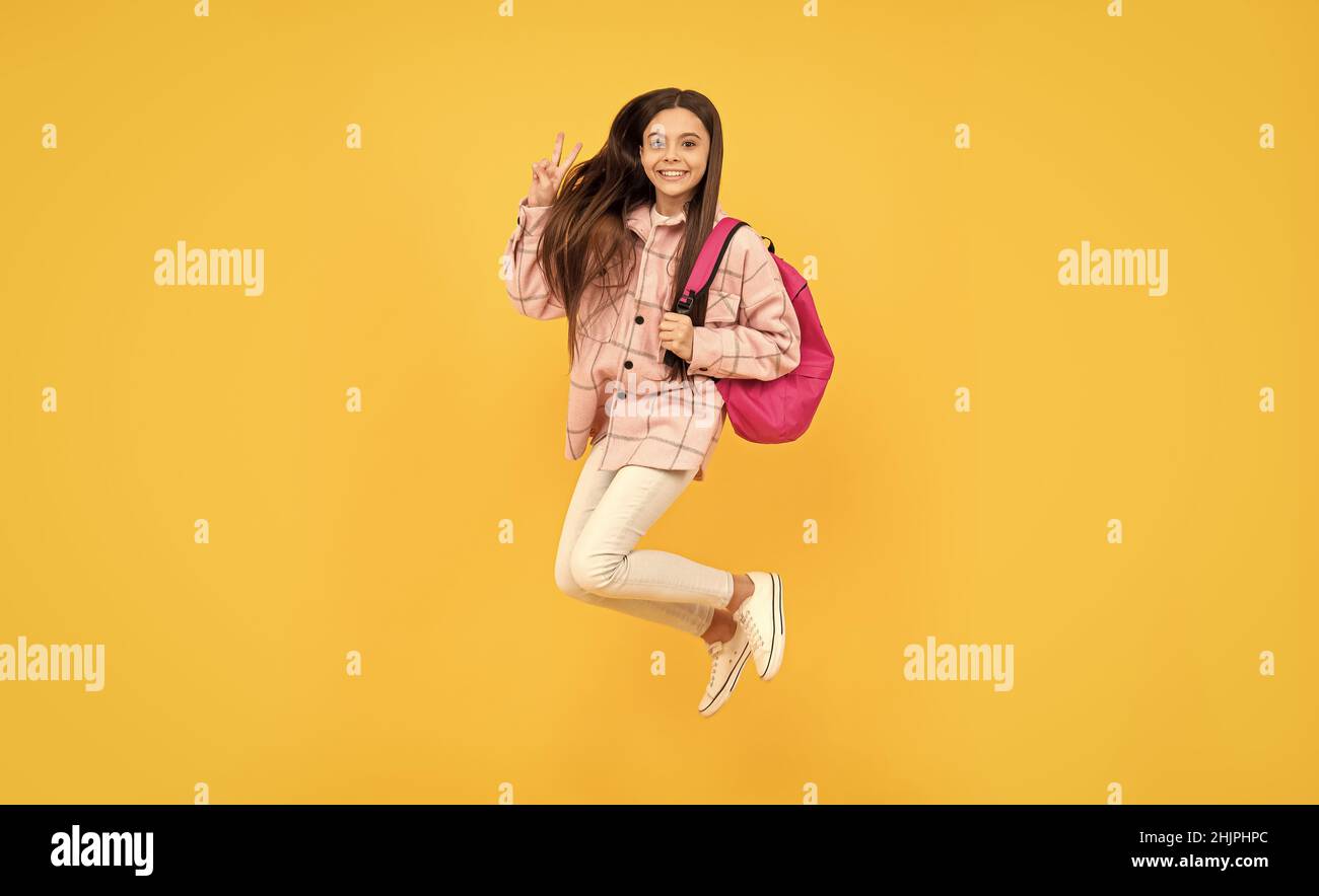 une jeune fille saute dans une chemise à carreaux. une course pour enfant heureuse avec sac à dos. un sac de transport pour enfant. Banque D'Images