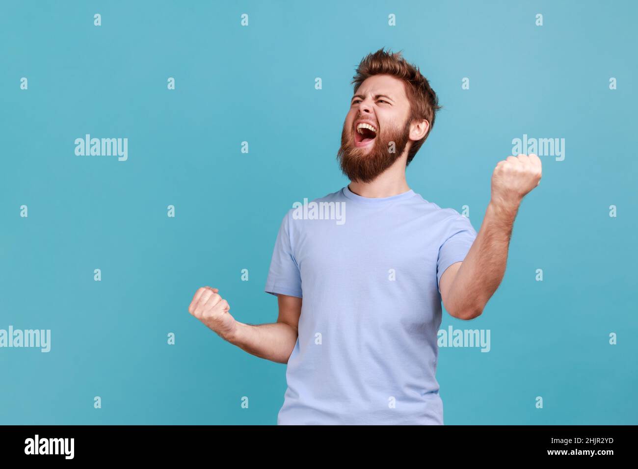 Portrait de l'homme barbu surjoyé debout avec une expression excitée, levant des poings, criant, criant oui, célébrant sa victoire,réussite.Studio d'intérieur isolé sur fond bleu. Banque D'Images Portrait de l'homme barbu surjoyé debout avec une expression excitée, levant des poings, criant, criant oui, célébrant sa victoire,réussite.Studio d'intérieur isolé sur fond bleu. Banque D'Images