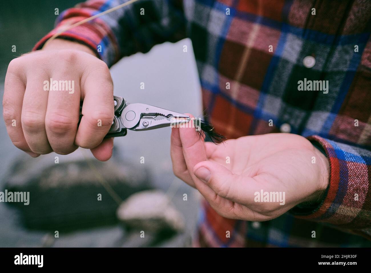 Un pêcheur de mouche utilise des pinces pour ajouter du poids à une mouche. Banque D'Images