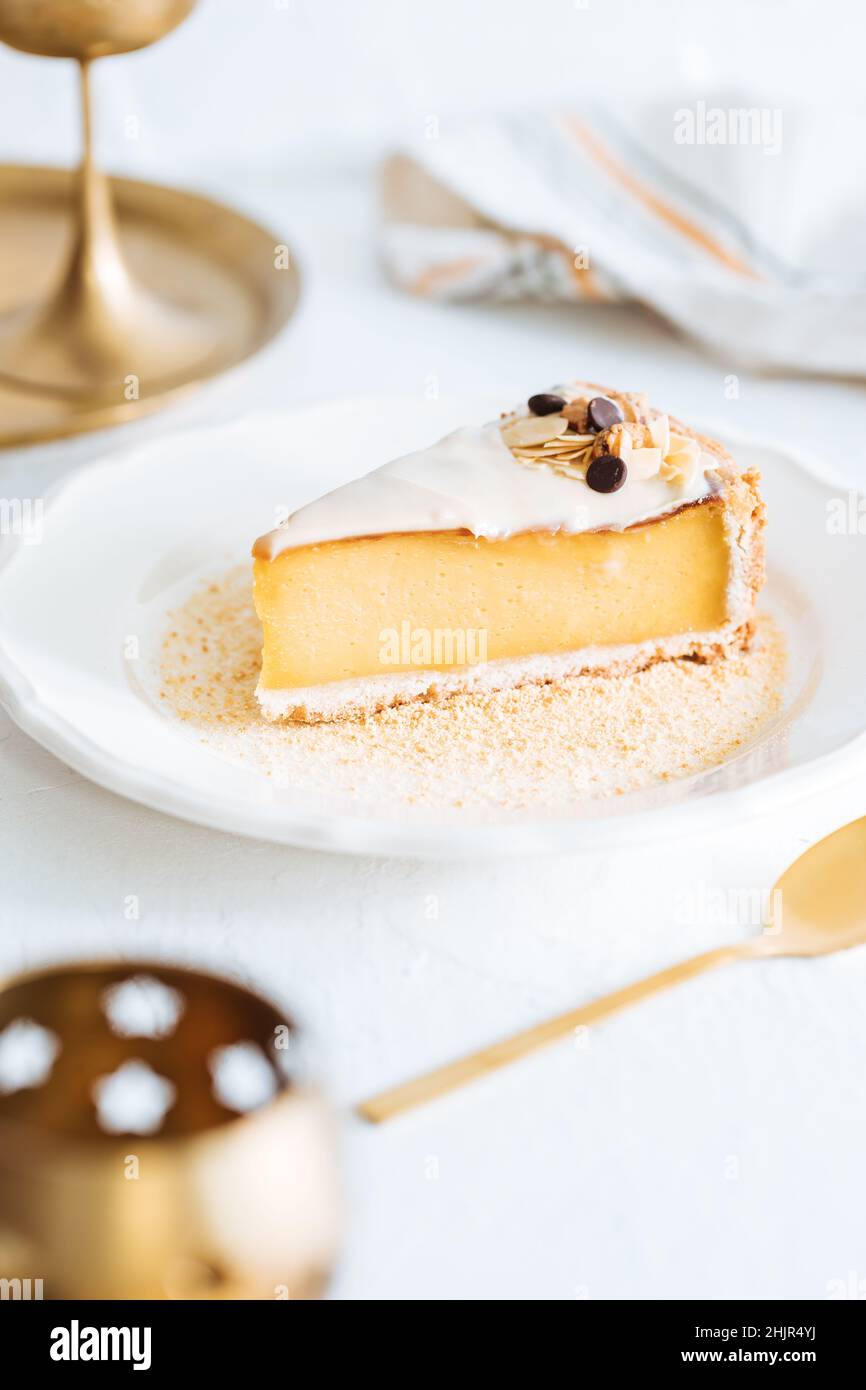 Flan français sur plaque blanche avec chapelure de biscuit autour, avec amandes sur le dessus.Gâteau sur fond blanc lumineux, dessert français traditionnel Banque D'Images