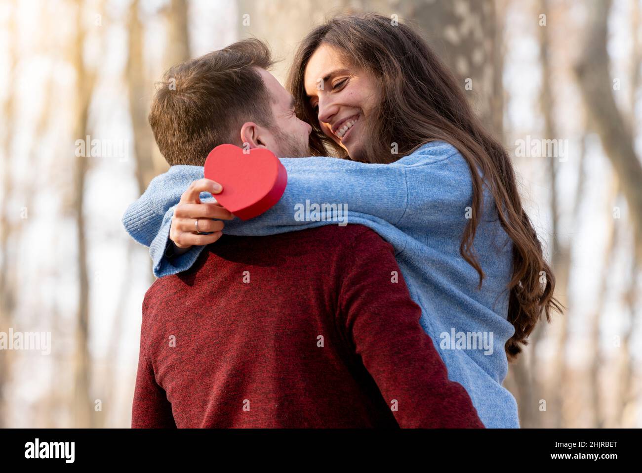 L'homme surprend sa petite amie avec un cadeau en forme de cœur et elle l'embrasse Banque D'Images